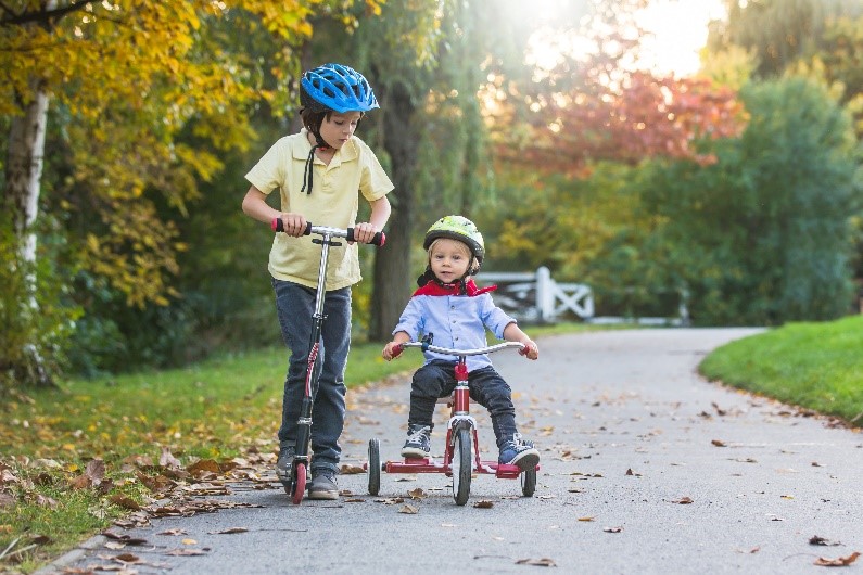 two boys riding a scooter and a bike